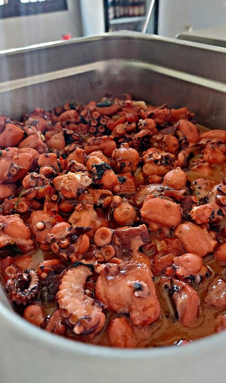 Polpo a pezzi in umido con sugo rosso ed erbe in una vaschetta d'acciaio sul banco di Al Gusto Giusto