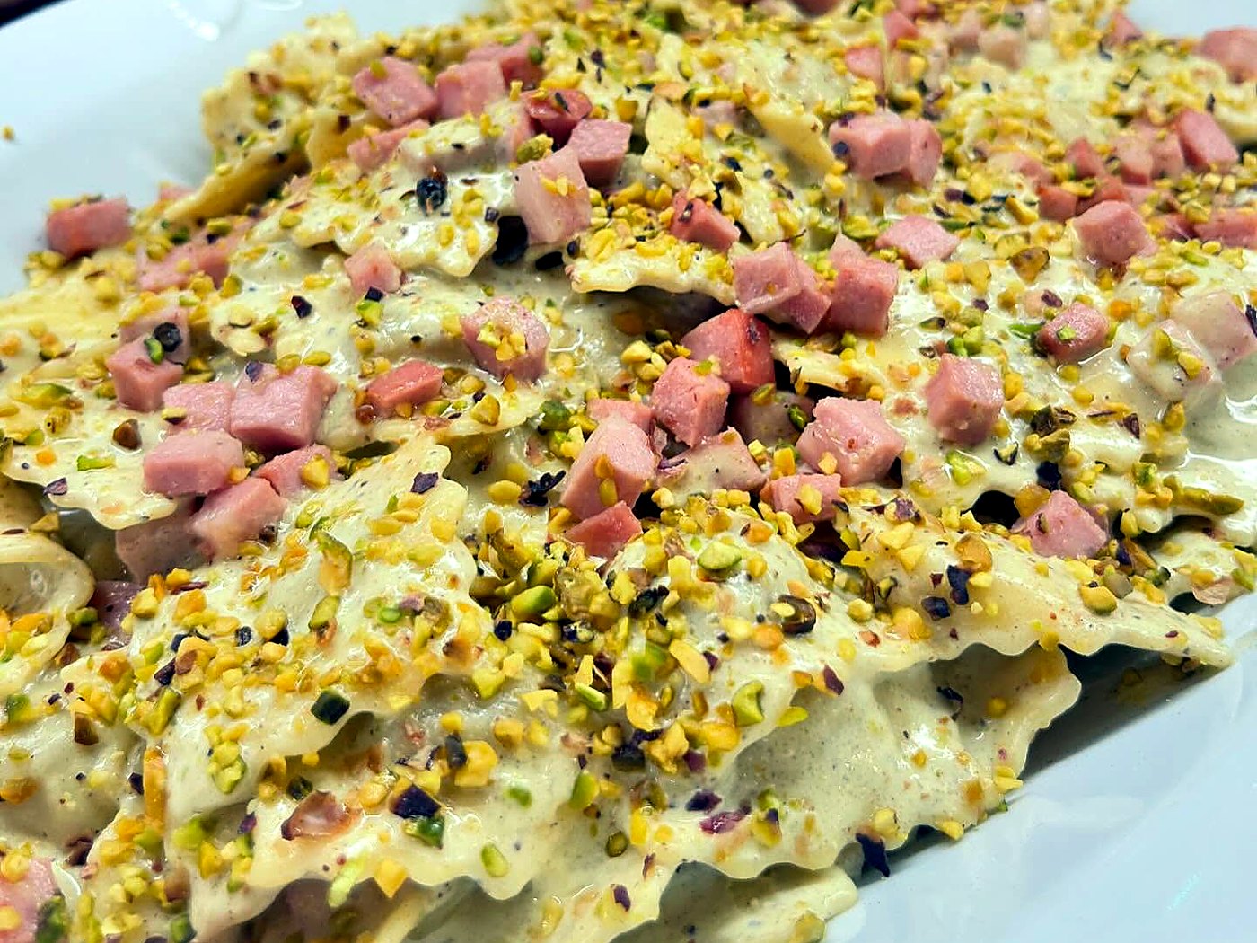 Ravioli dal bordo ondulato in crema chiara con cubetti di salume e granella di pistacchio, piatto di Al Gusto Giusto